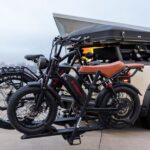 Electric bikes on car rack by a waterfront, illustrating outdoor adventures and modern travel.