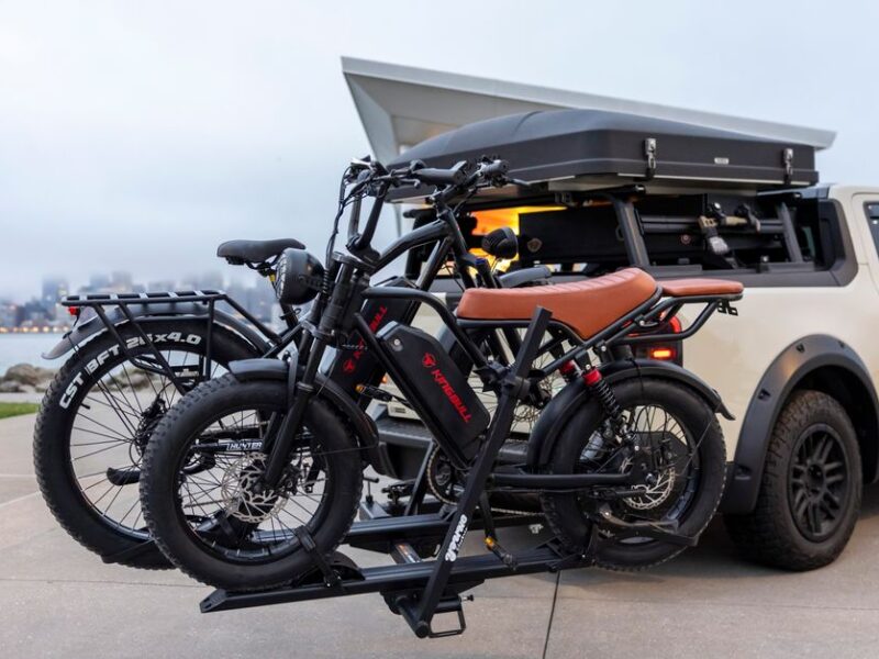 Electric bikes on car rack by a waterfront, illustrating outdoor adventures and modern travel.