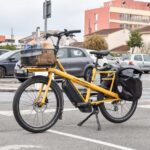 A yellow cargo e-bike carrying groceries parked outside a supermarket in France.